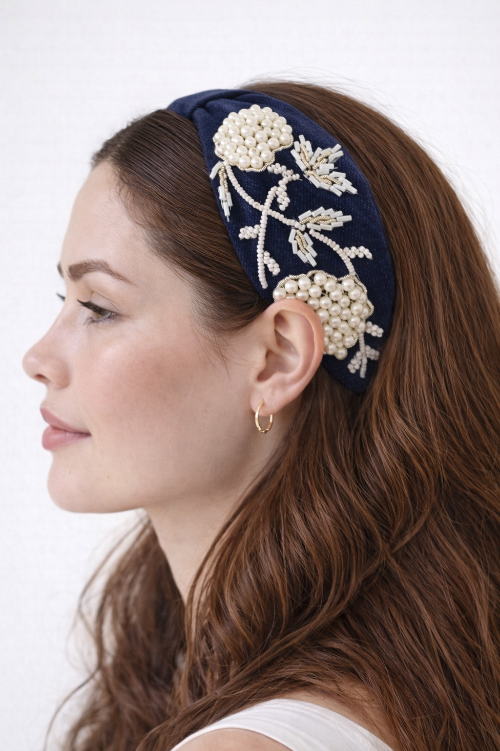 Woman wearing a denim headband with white floral embellishments on a white background