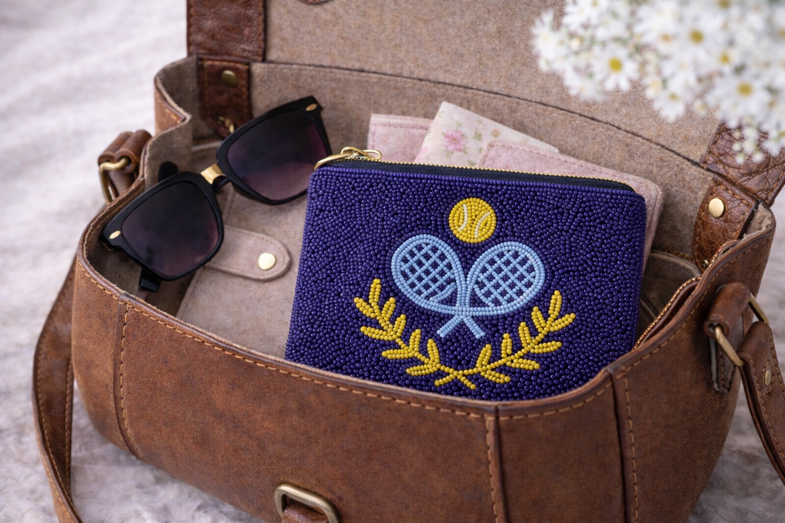 Brown leather bag with sunglasses and a blue pouch featuring a padel design.
