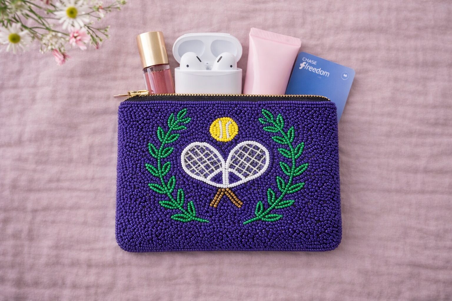 Beaded pouch with tennis design containing small items on a pink background