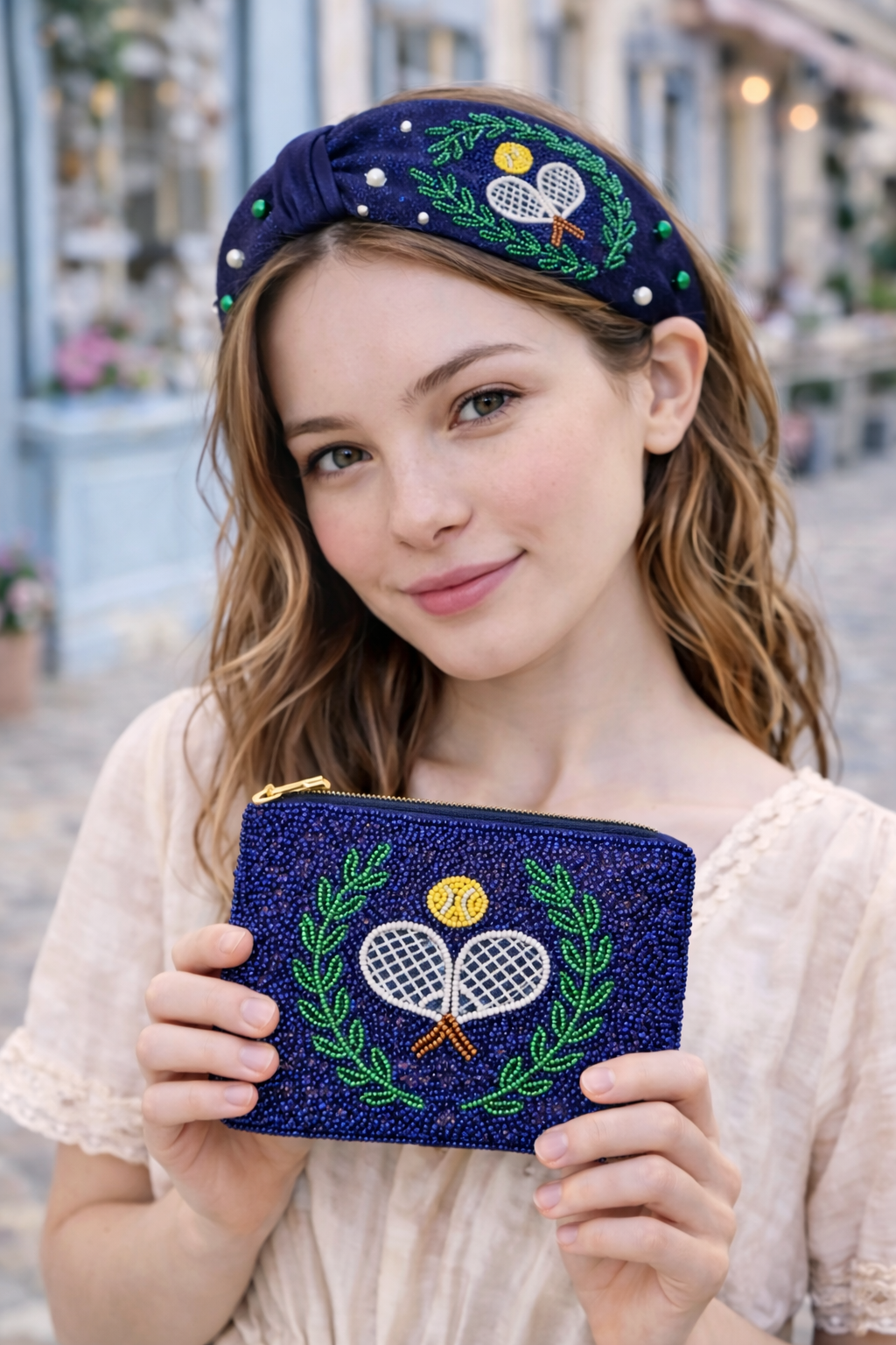 Woman holding a blue embroidered pouch wearing a matching headband with tennis design