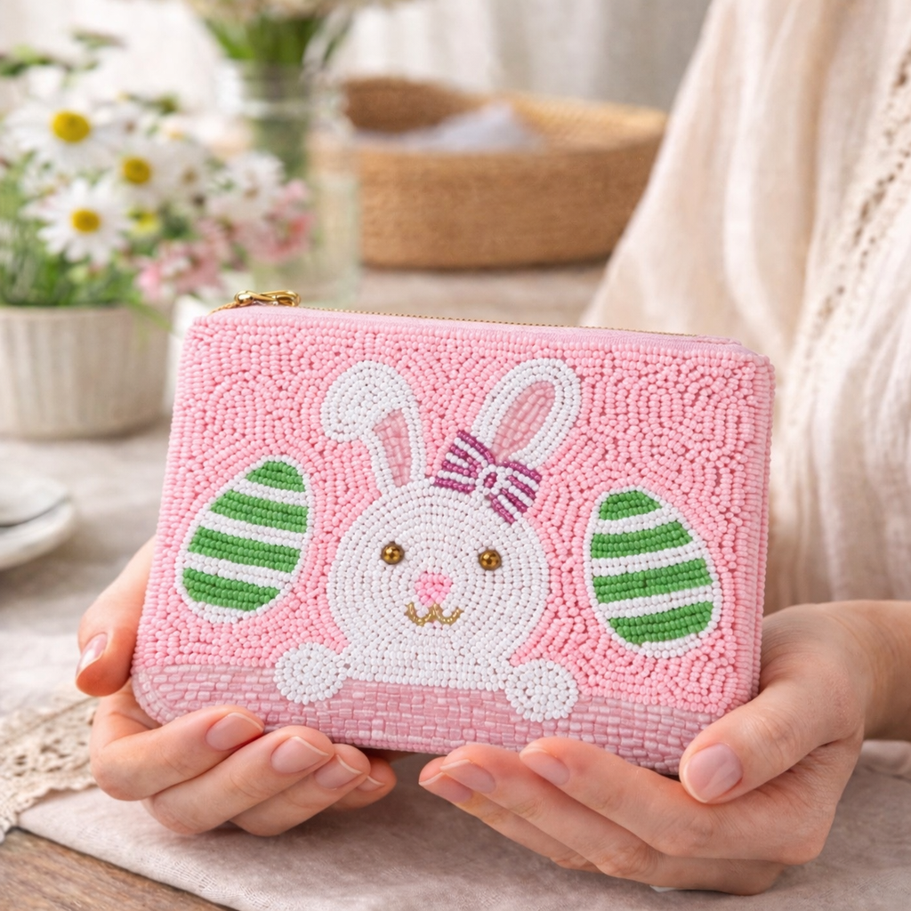 Pink beaded wallet with a bunny design held by hands on a table.