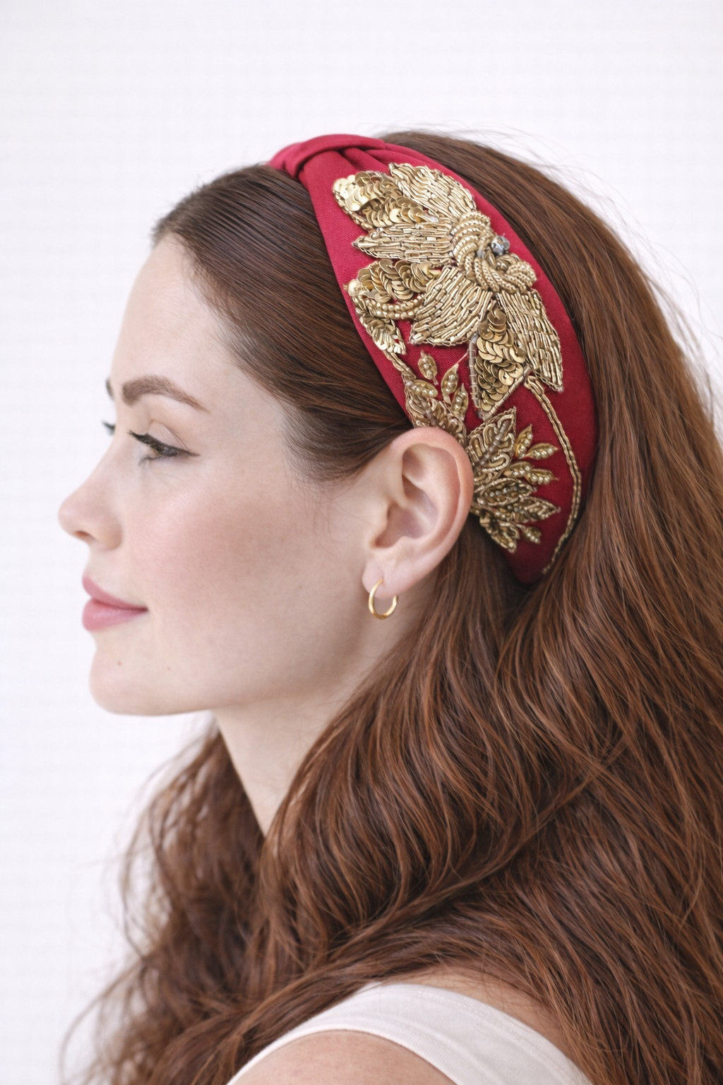 Woman wearing a fuschia pink headband with gold leaf designs on a white background