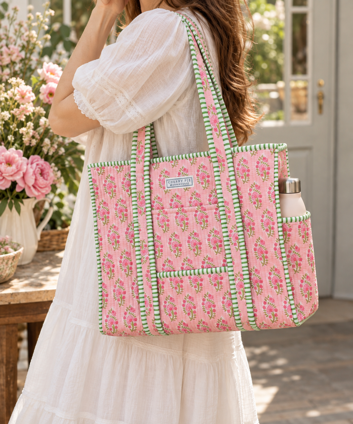 Pink floral quilted tote with green striped trim carried over the shoulder in a cottage garden setting