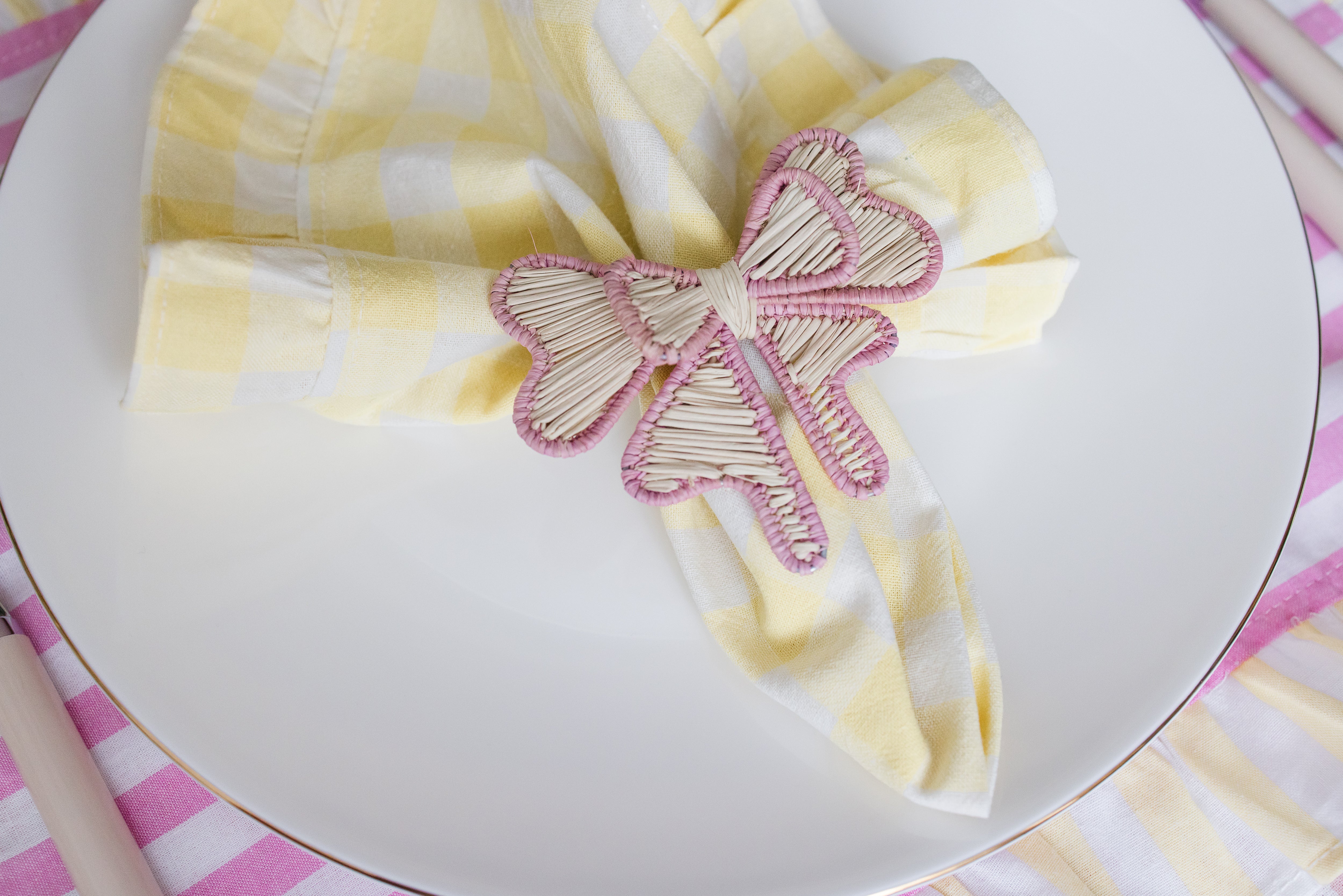 Handcrafted iraca palm bow napkin rings in pink wrapped around linen napkins on table