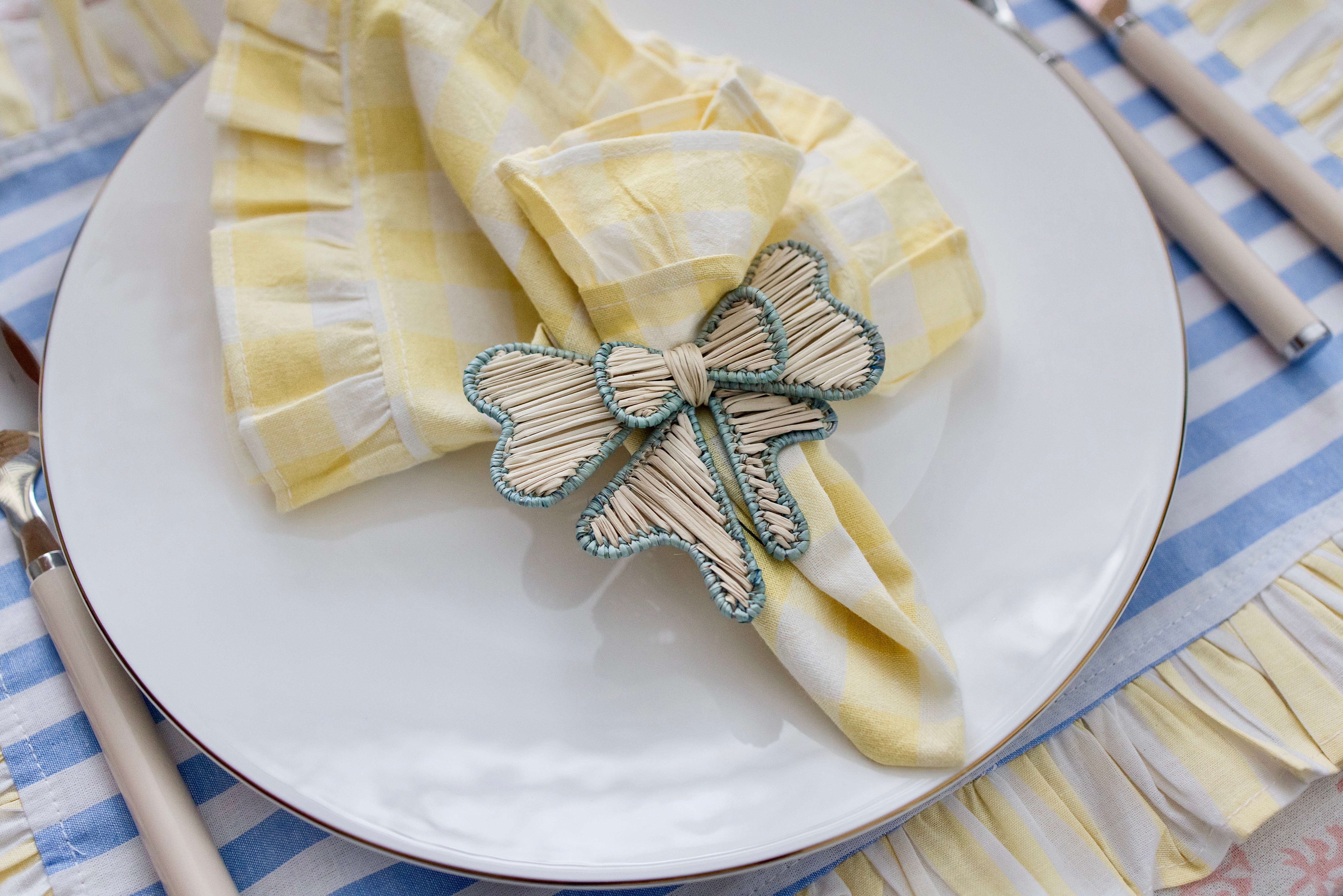 Handcrafted iraca palm bow napkin rings in blue wrapped around linen napkins on table