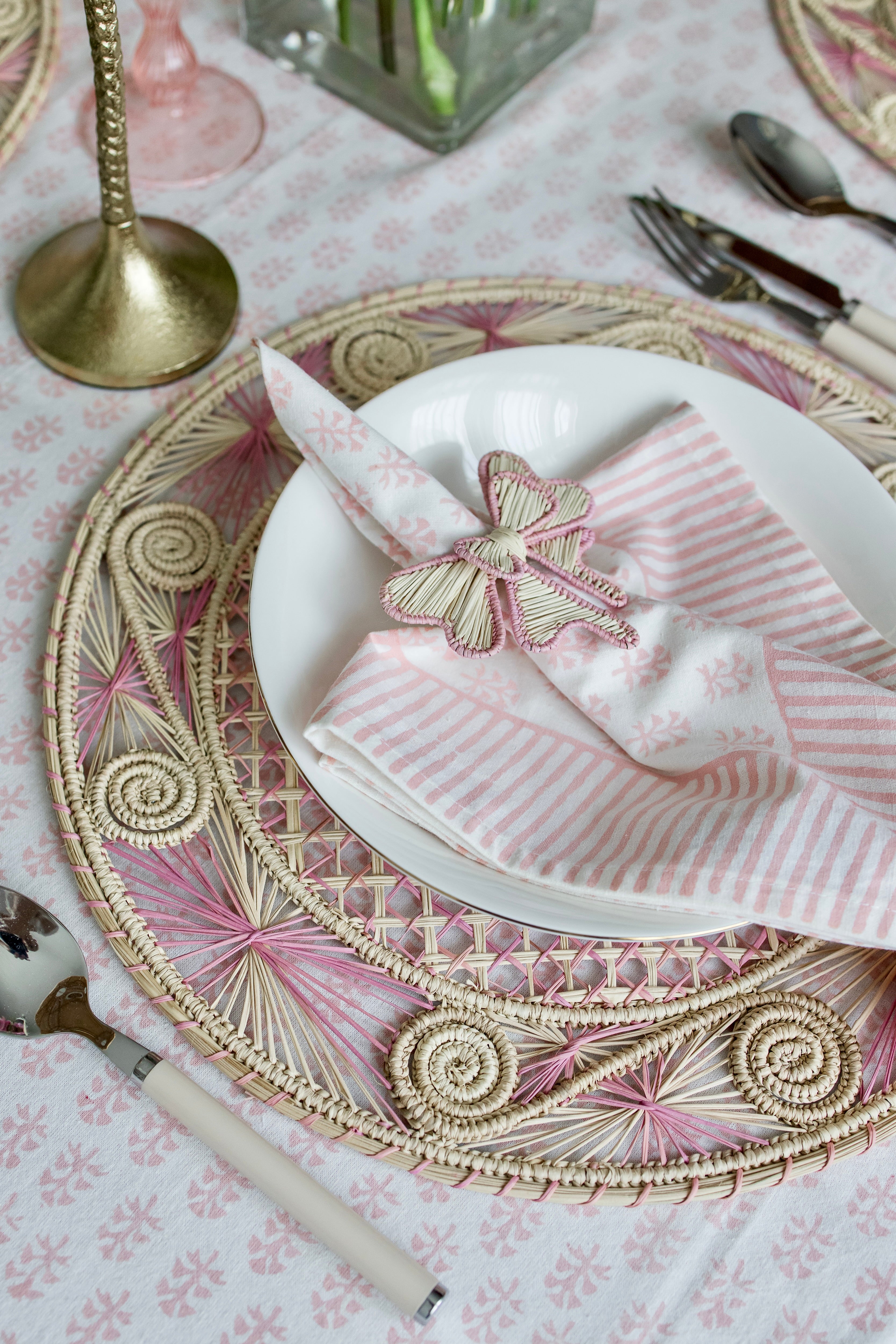 Handcrafted iraca palm bow napkin rings in pink wrapped around linen napkins on table