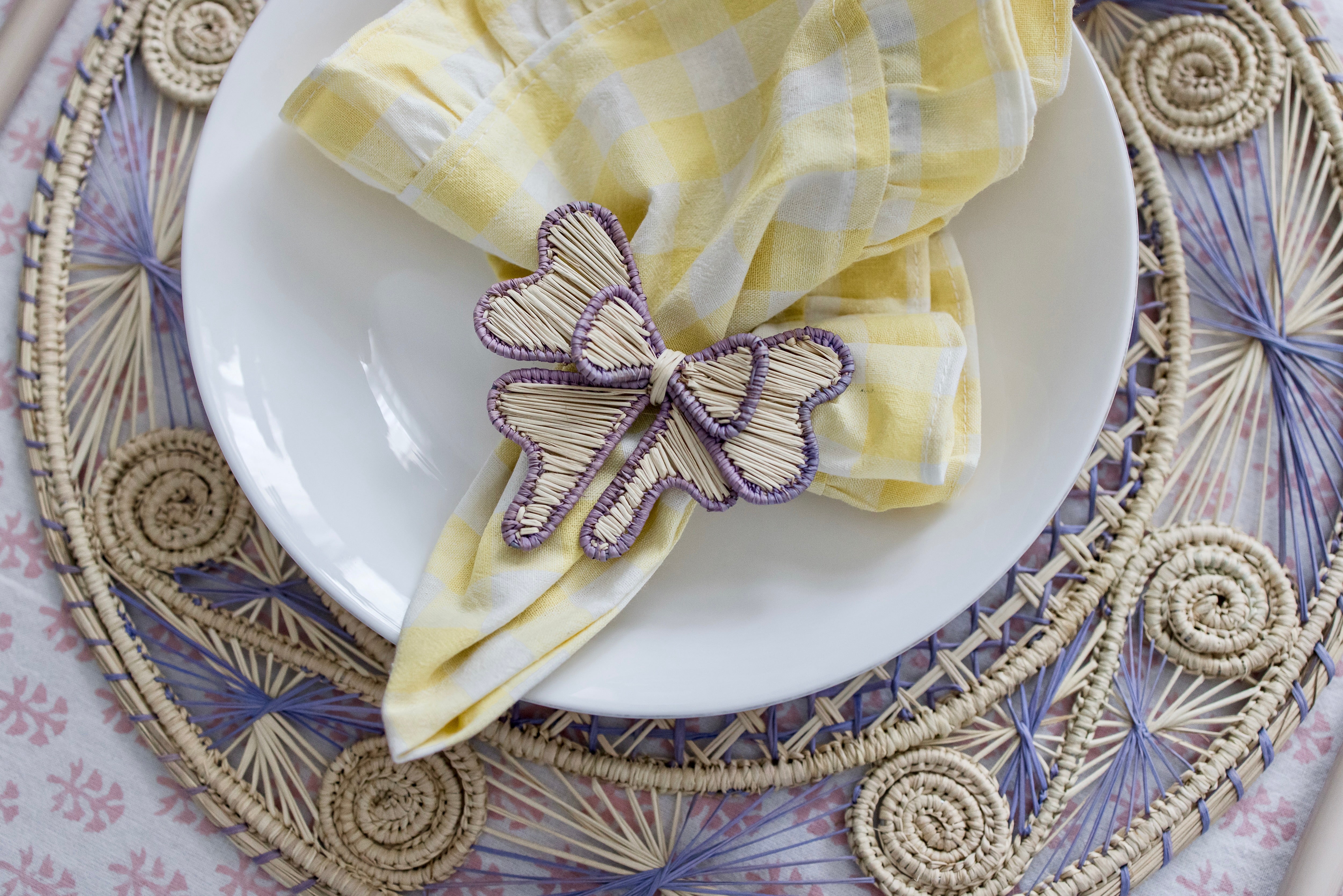 Handcrafted iraca palm bow napkin rings in purple lavender wrapped around linen napkins on table