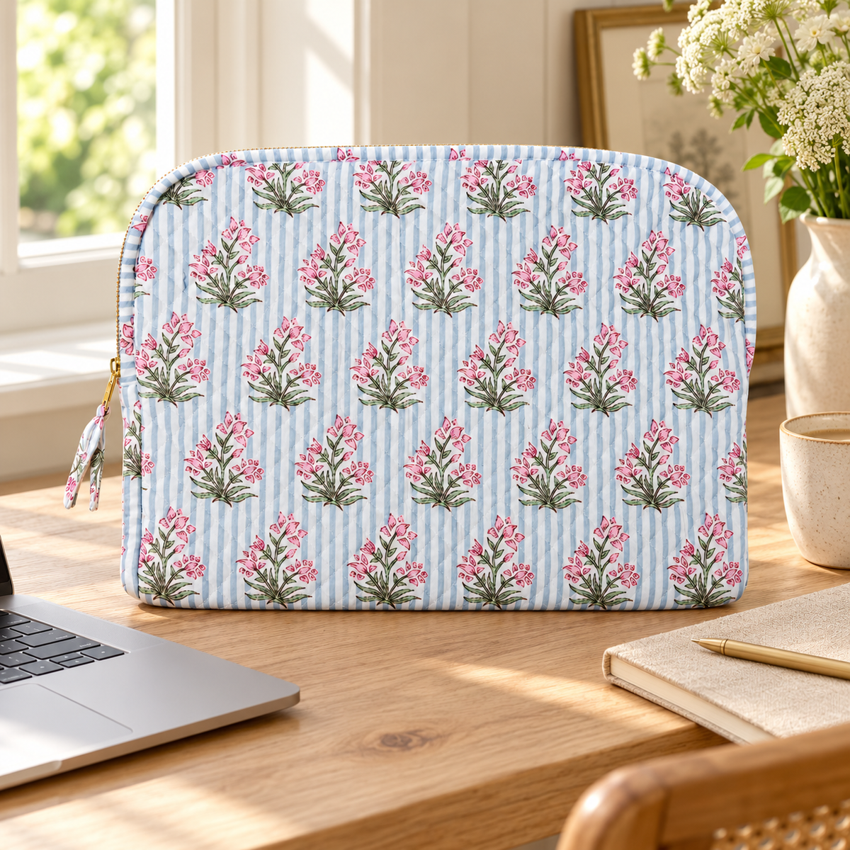 Cornflower blue striped floral laptop sleeve styled on a sunlit pale wood desk