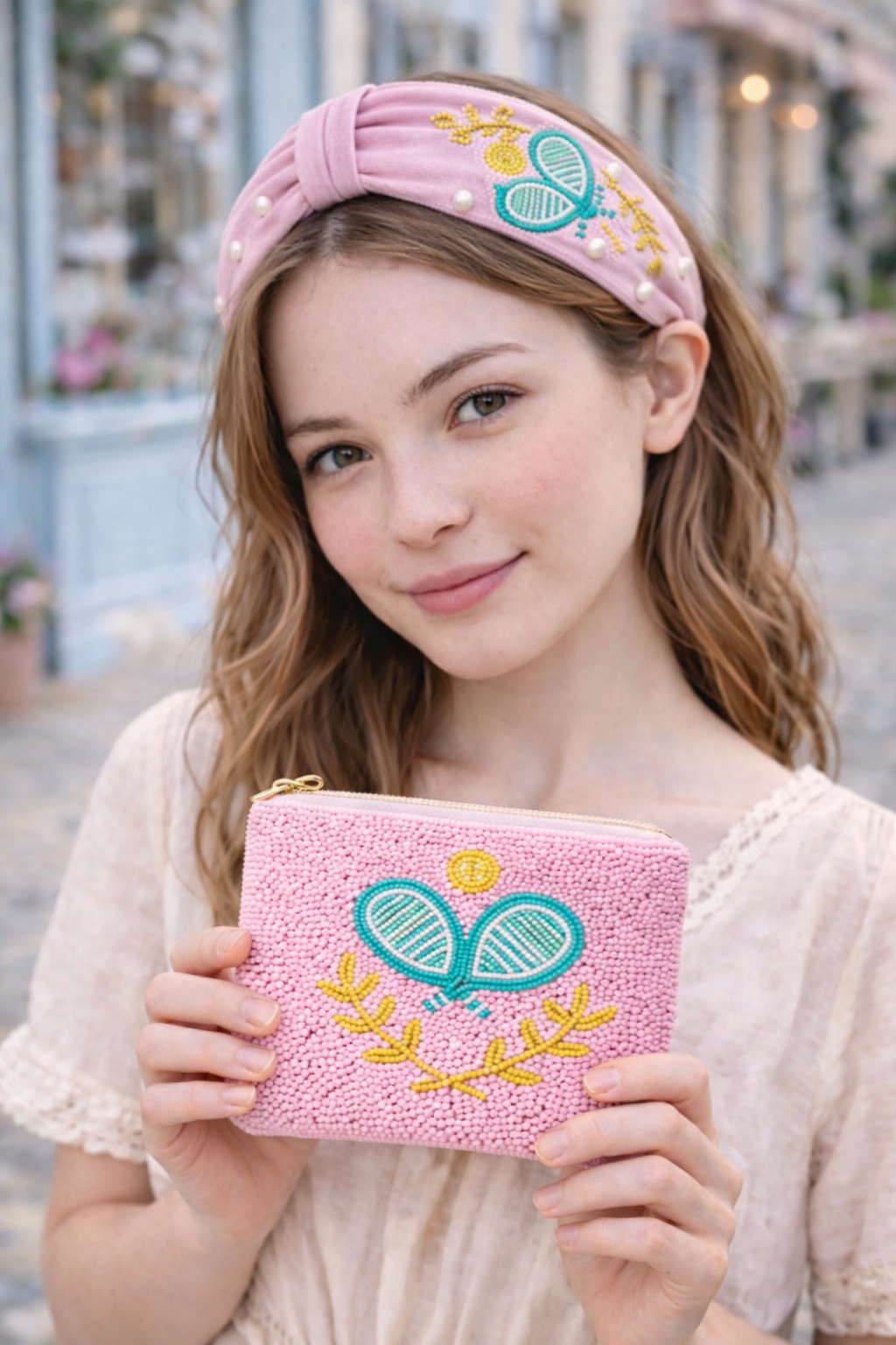 Woman holding a pink embroidered pouch wearing a matching headband with a pickleball design