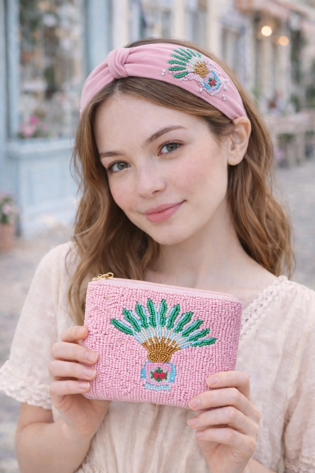 Woman holding a pink beaded pouch and wearing a matching headband with pink traveller's palm and peranakan motif design