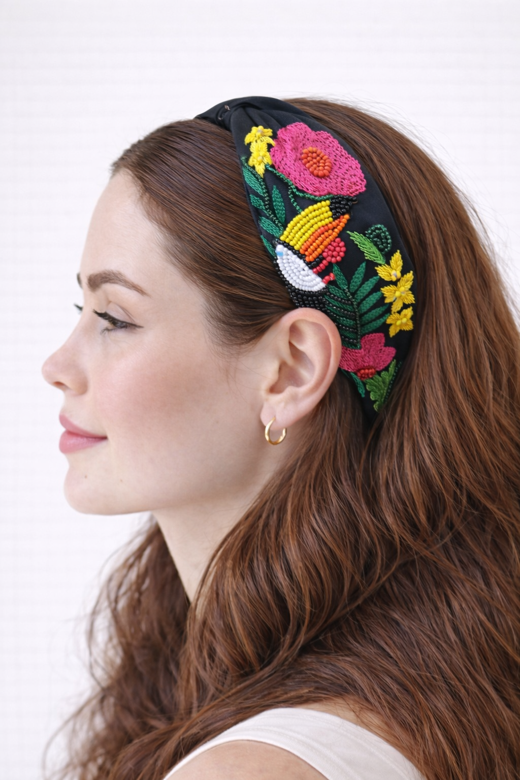 Woman wearing a colorful embroidered headband with flowers and toucan on a white background