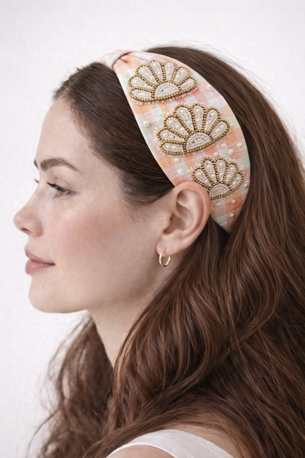 Woman wearing a decorative headband with beaded seashells on multi-colour gingham fabric.