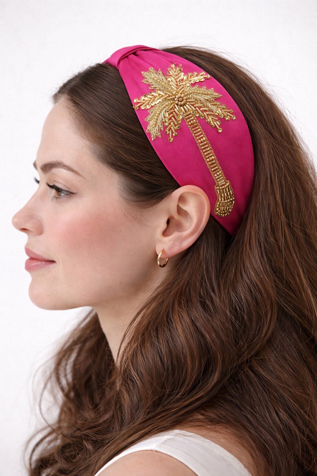 Woman wearing a pink headband with gold palm tree design on a white background