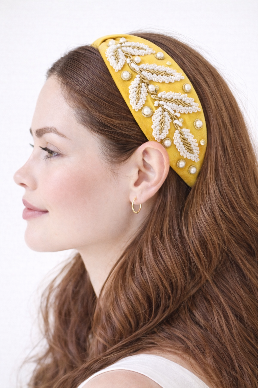 Woman wearing a yellow headband with white leaf patterns on a white background
