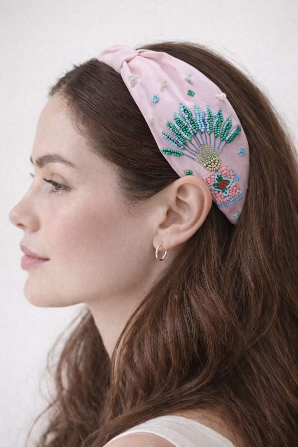 Woman wearing embroidered headband with traveller palm design and peranakan motif on a white background