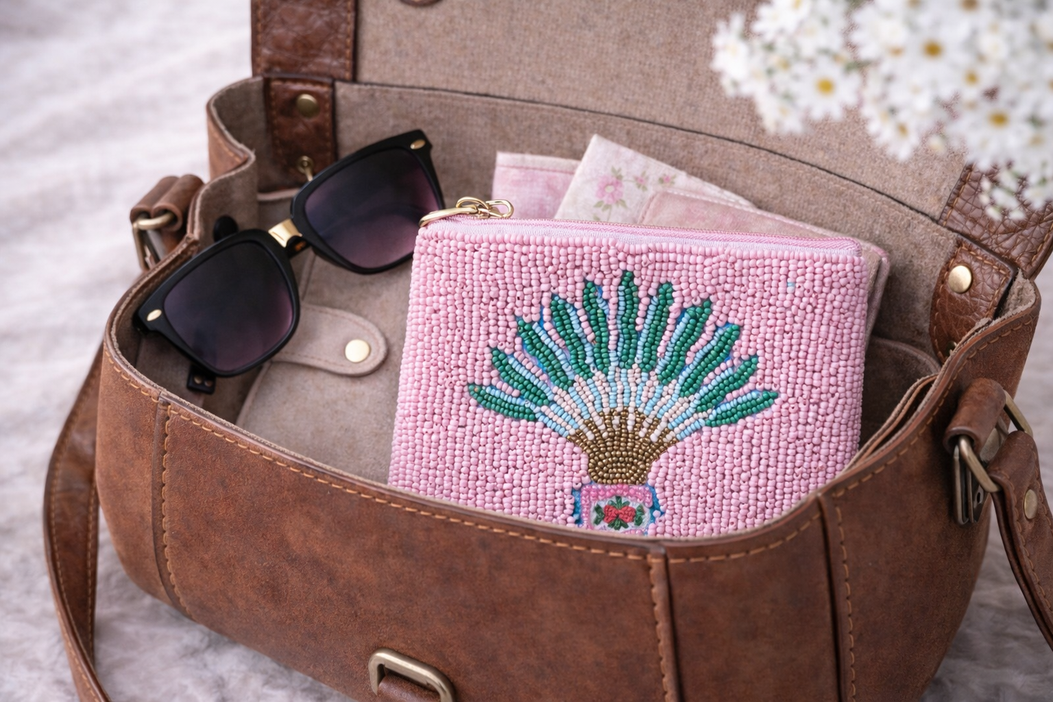 Brown leather bag with sunglasses and a pink beaded pouch inside