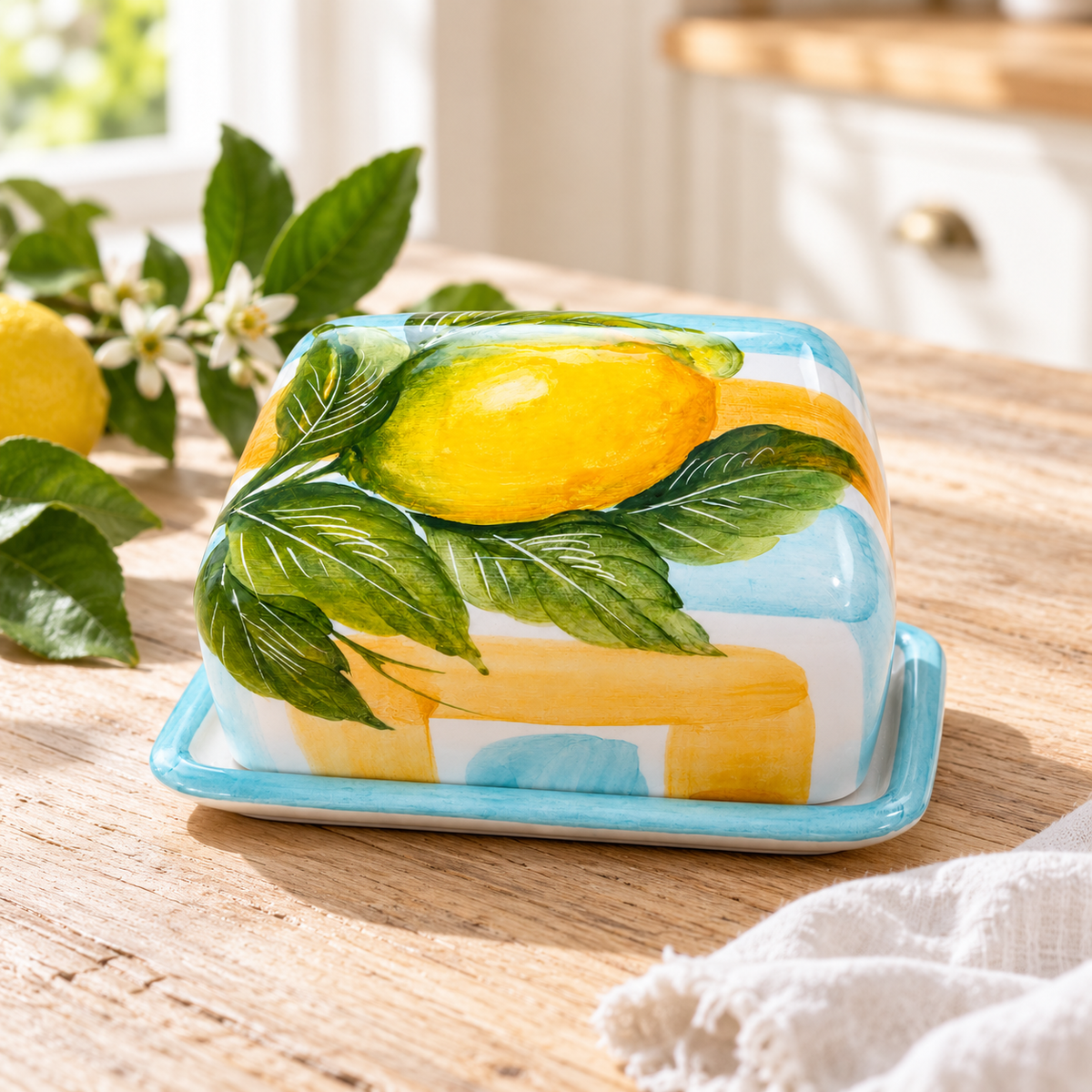 Lemon-painted ceramic butter dish styled on a sunlit farmhouse kitchen table with fresh lemon leaves.